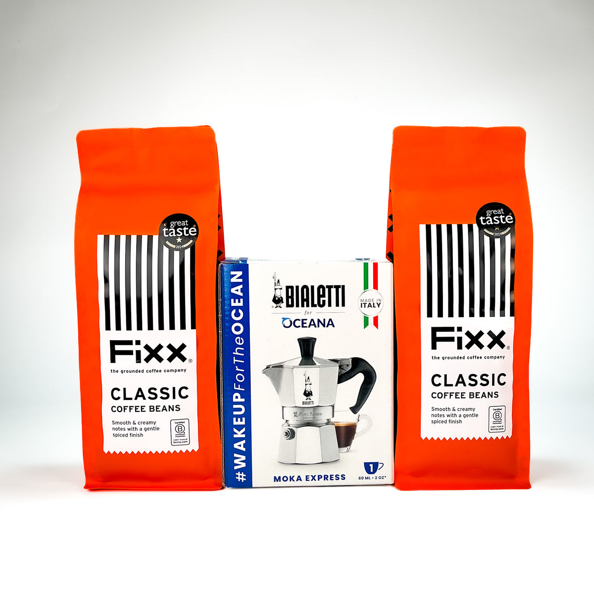 Two orange bags of Fixx Classic Coffee Beans flanking a white and blue Bialetti Oceana Moka Express coffee maker box, set against a clean white background.