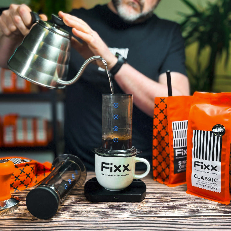 Person pouring coffee into a Fixx coffee maker with Fixx coffee bags in the background.