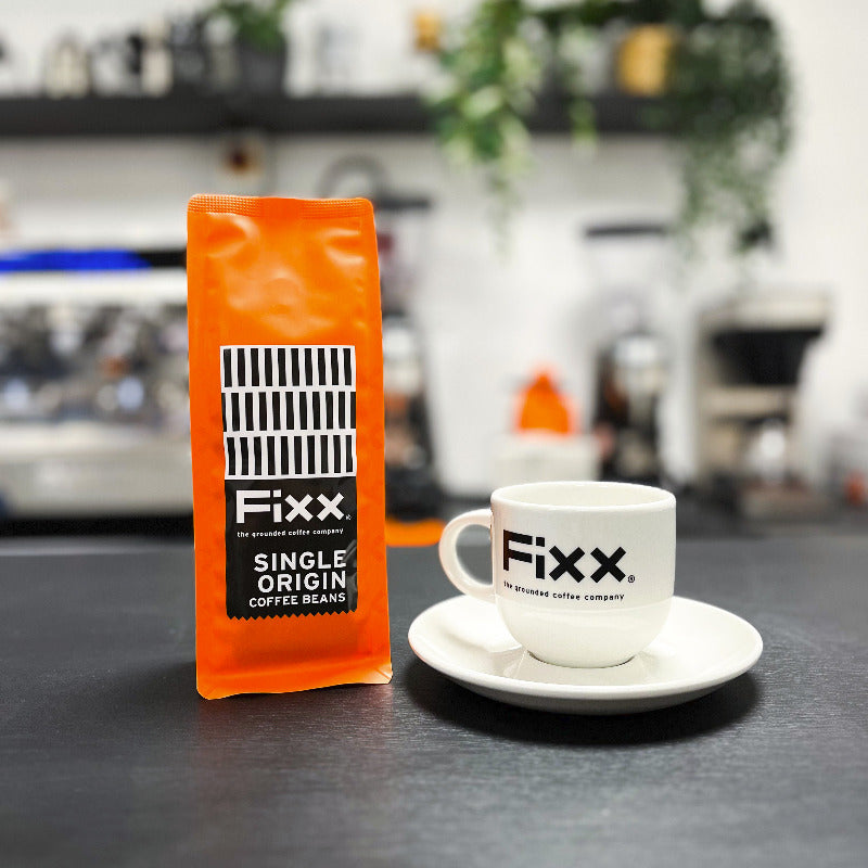 Fixx coffee package and cup on a dark surface with a blurred background