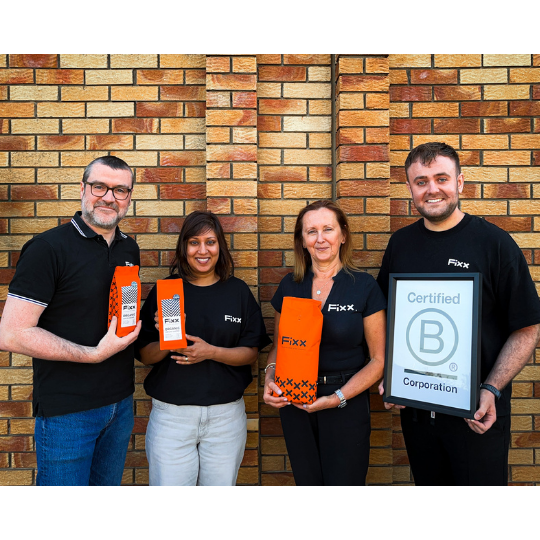 Four people holding orange and black packaging and a framed certificate against a brick wall.