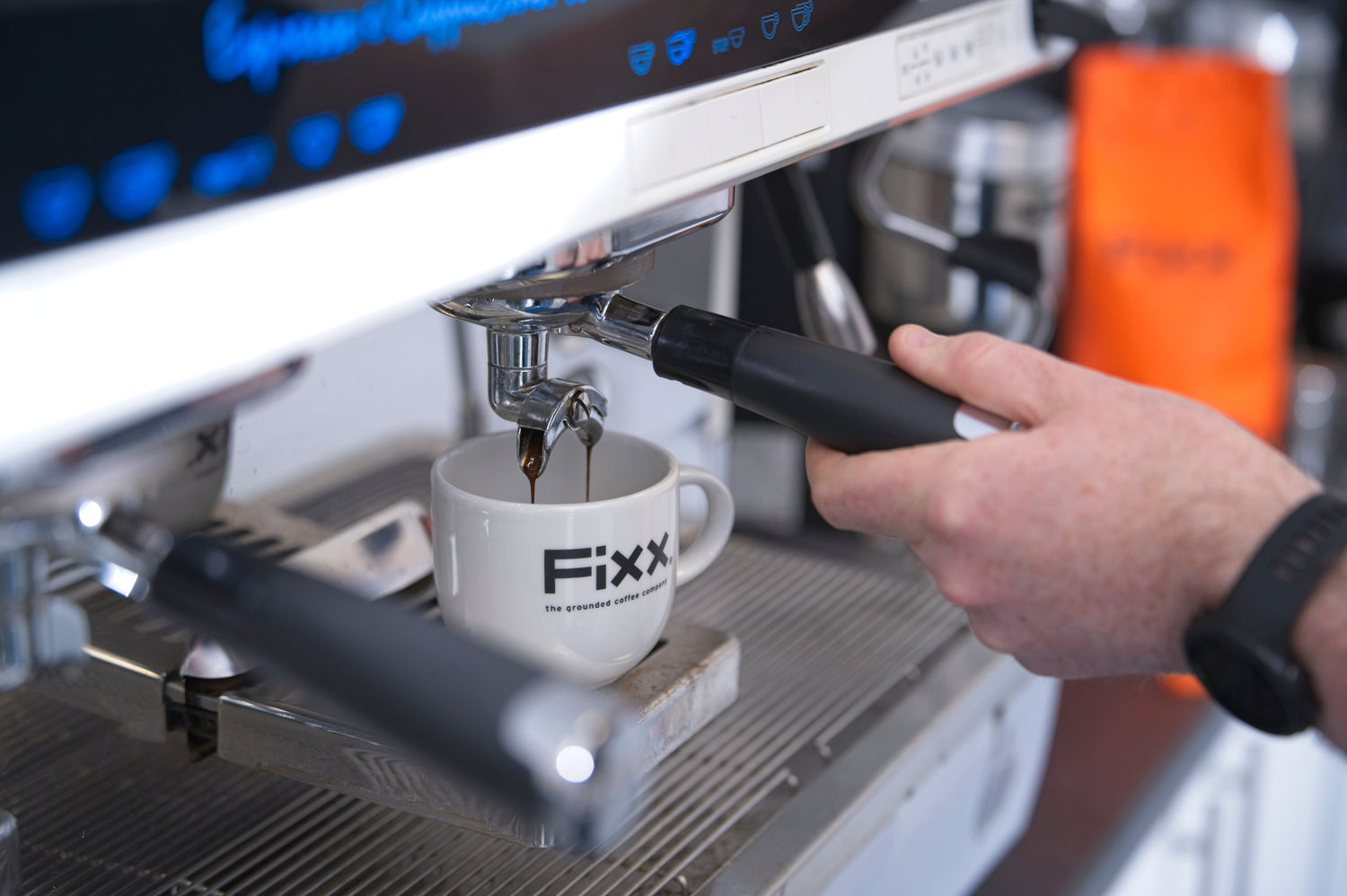 Espresso pouring into a white FiXX coffee cup while a hand holds the coffee machine handle.
