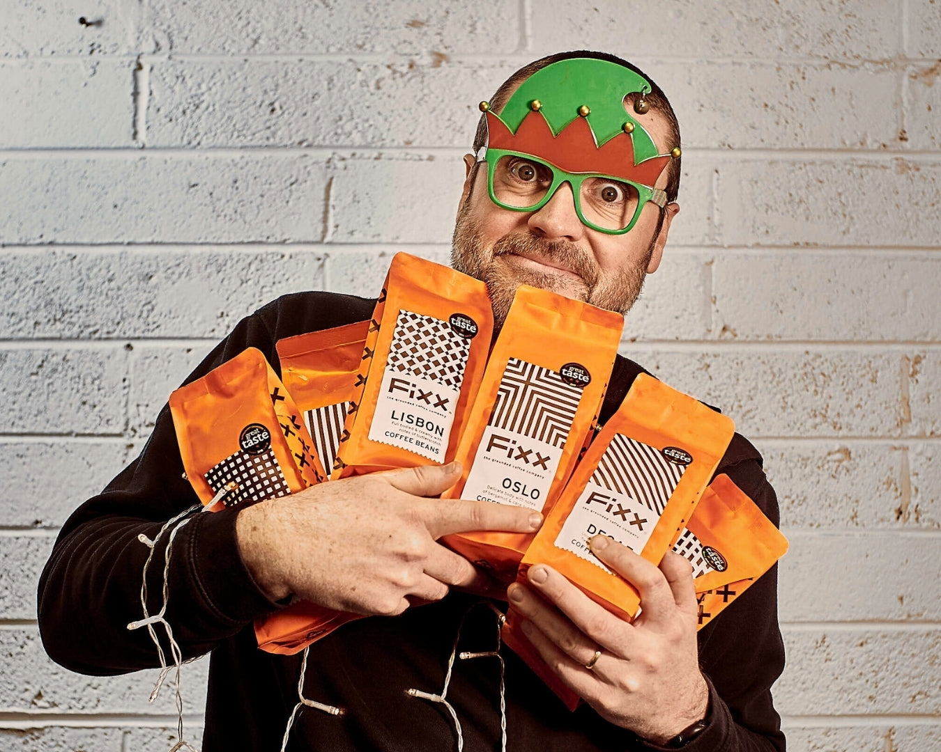 A man holding a selection of FiXX Coffee while wearing green elf glasses