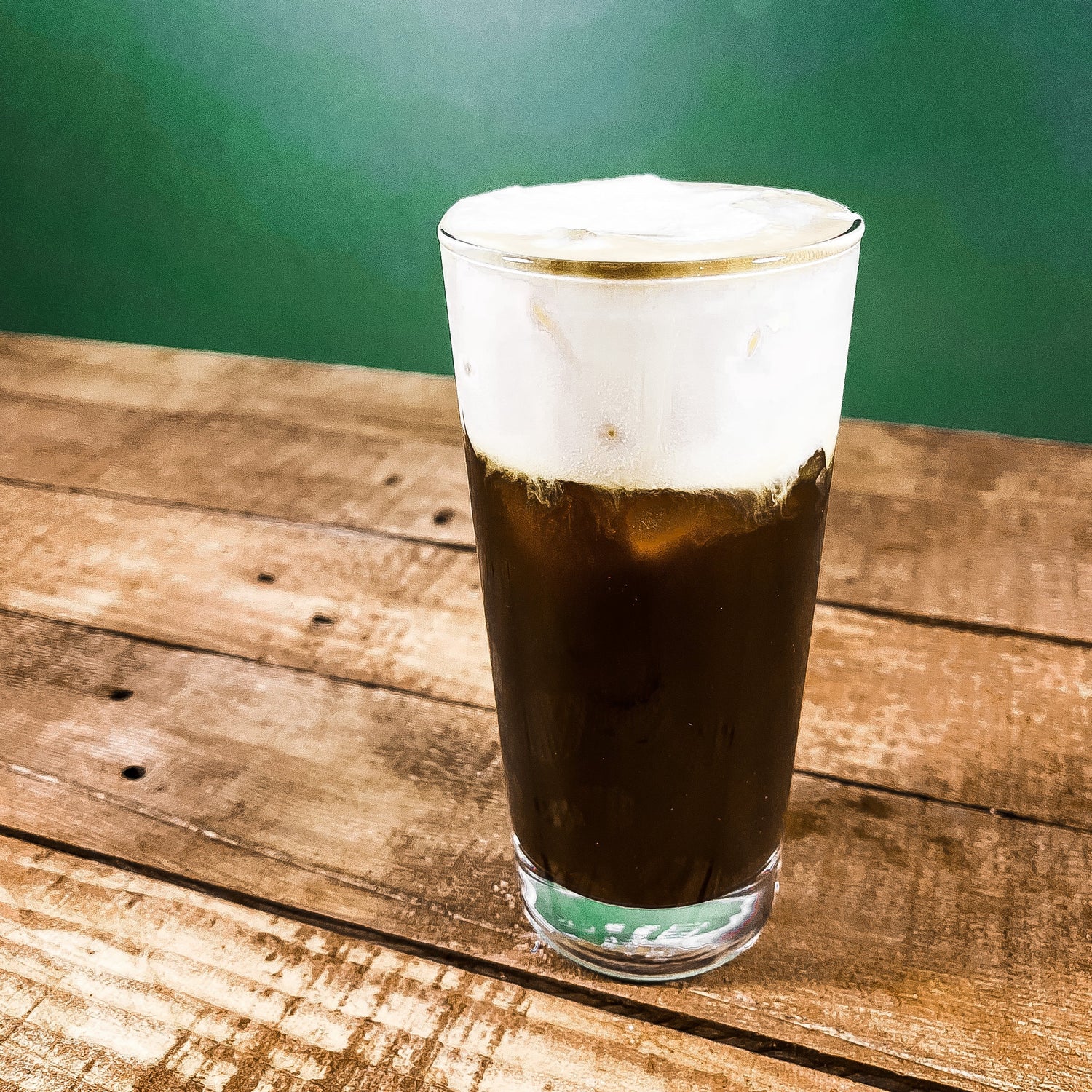 A glass of Iced Irish Coffee cocktail on a wooden table with a green background.
