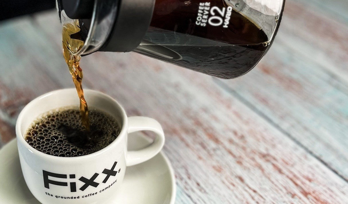 A Hario V60 decanter pouring pour-over brewed coffee into a FiXX Coffee mug.