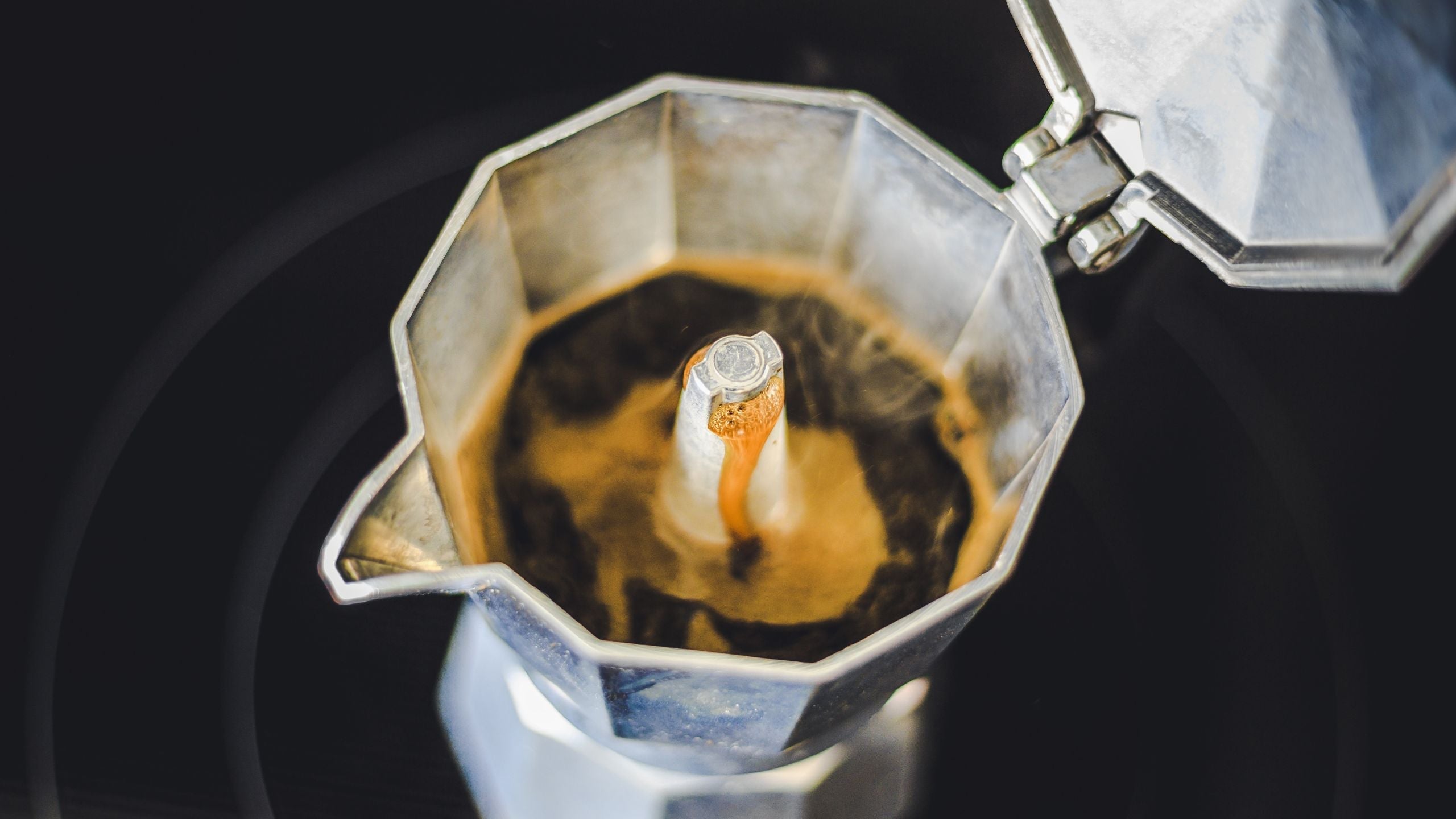 A close up photo of a Bialetti Moka pot brewing coffee on a stovetop. 