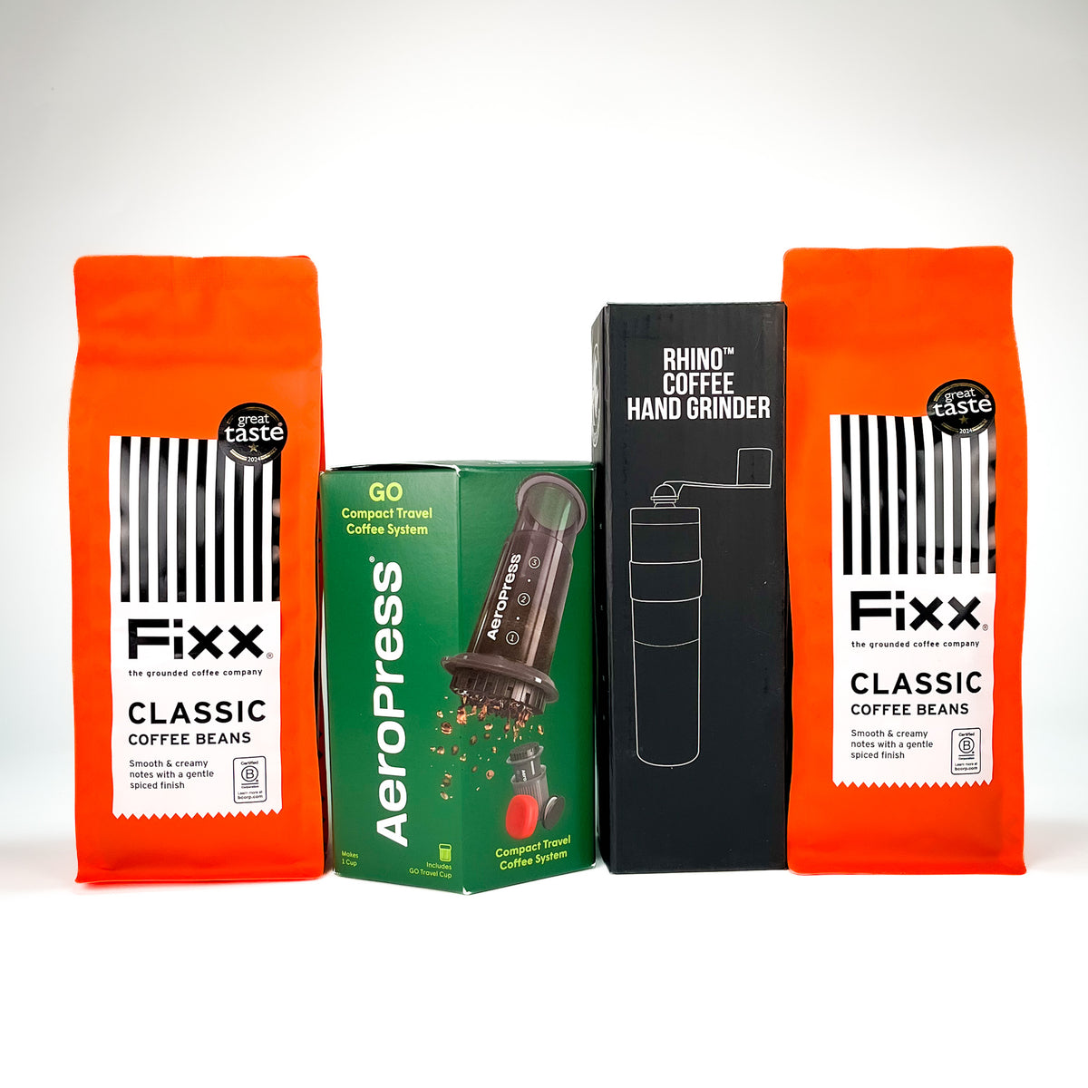 A product bundle featuring two bags of Fixx Classic Coffee Beans in bright orange packaging, a green AeroPress travel coffee system box, and a black Rhino Coffee Hand Grinder box, arranged against a clean white background.