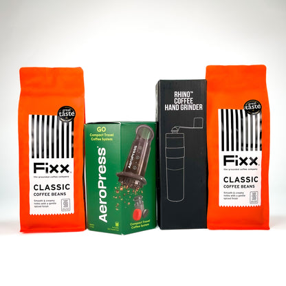 A product bundle featuring two bags of Fixx Classic Coffee Beans in bright orange packaging, a green AeroPress travel coffee system box, and a black Rhino Coffee Hand Grinder box, arranged against a clean white background.