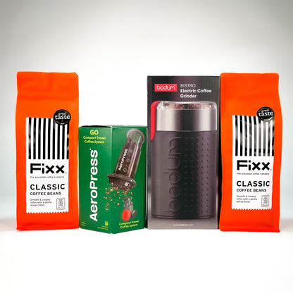 A product bundle featuring two bags of Fixx Classic Coffee Beans, a green AeroPress coffee maker box, and a black Bostik electric coffee grinder in its retail packaging, arranged against a light gray background.