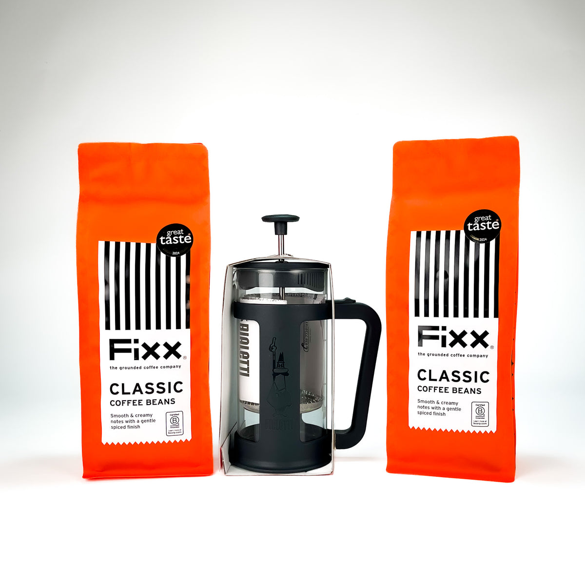 Two bright orange bags of Fixx Classic Coffee Beans flanking a black and glass French press, arranged symmetrically on a clean white background.