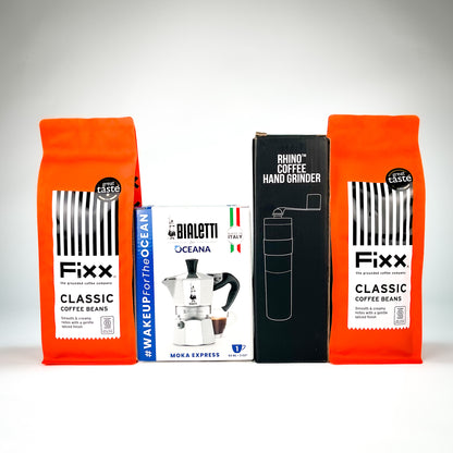 A coffee gift set featuring two bright orange bags of Fixx Classic Coffee Beans, a white and blue Birrelli Oceana moka pot, a black Rhino Coffee Hand Grinder box, and a white coffee cup, arranged on a light gray background.