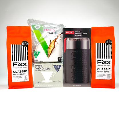 A coffee-related product bundle on a light gray studio background, including two orange bags of Fixx Classic Coffee Beans, a package of Mario V60 dripper, and a boxed Boudin Bistro Electric Coffee Grinder.