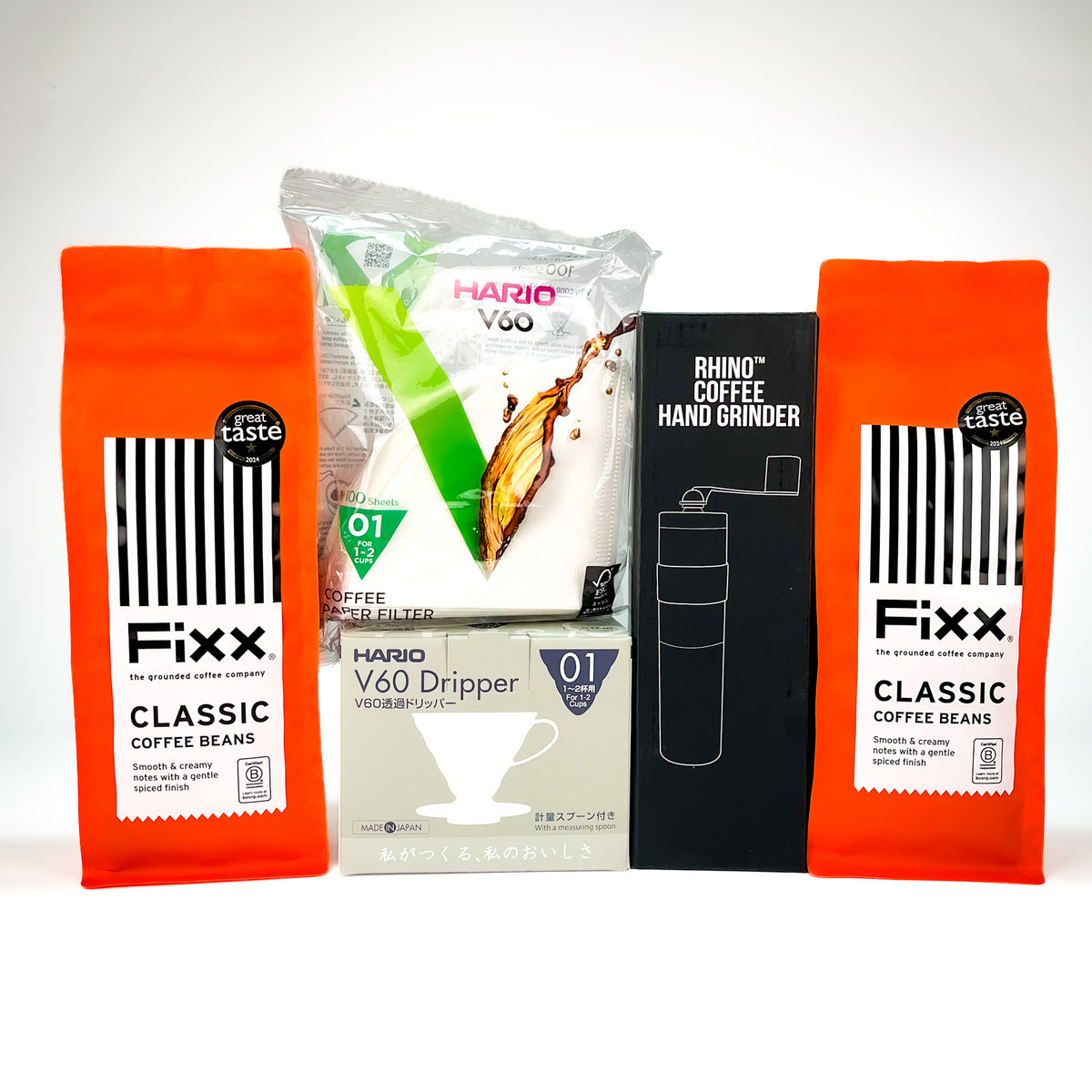 A coffee gift set featuring two orange bags of Fixx Classic Coffee Beans, a bag of Hario V60 dripper, a black box of a Rhino hand grinder, and a gray box of Hario V60 V60i W20, arranged on a white background.