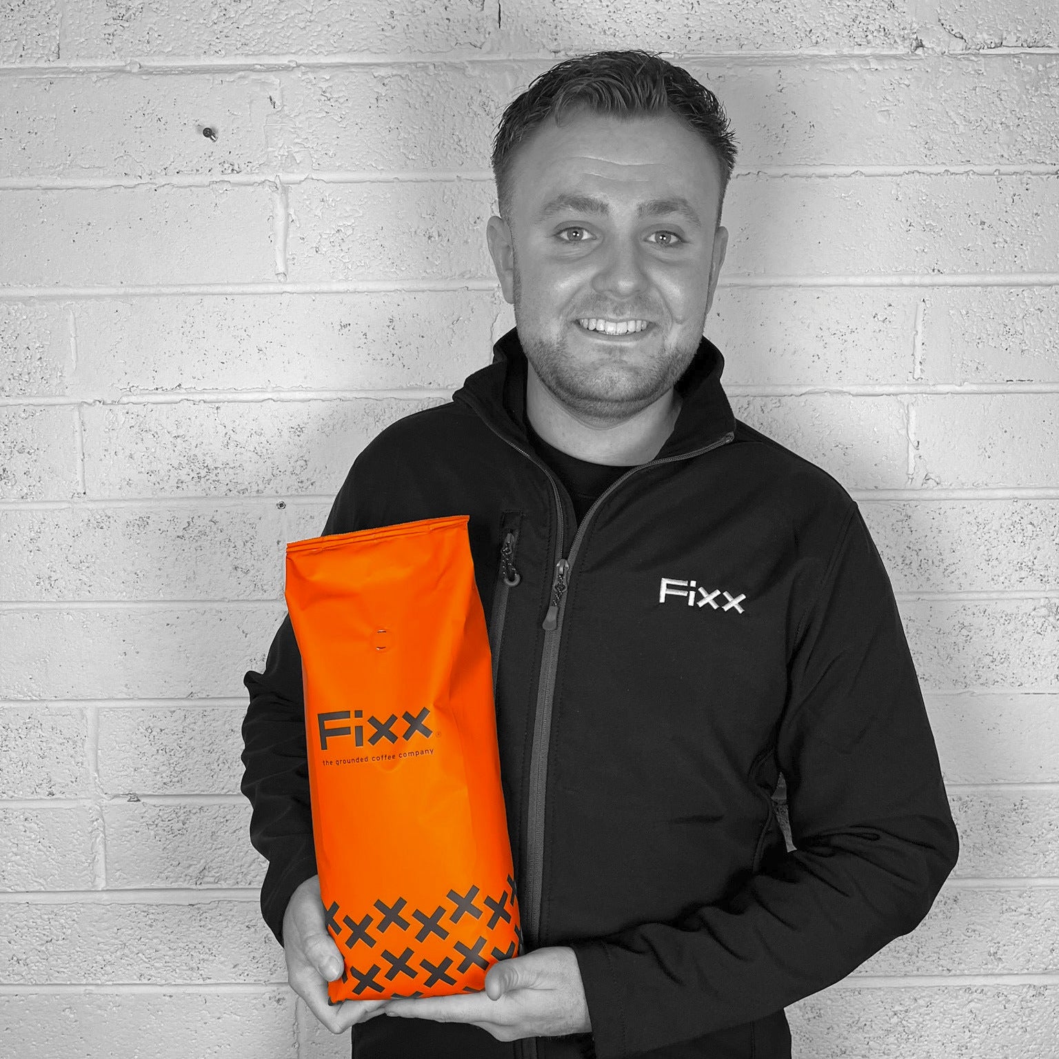 Man holding an orange 'Fixx' bag against a gray brick wall