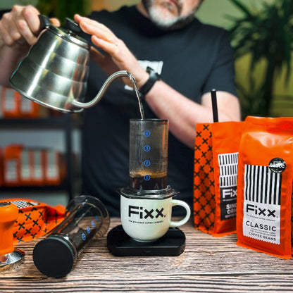 Person pouring coffee into a Fixx coffee maker with Fixx coffee bags in the background.