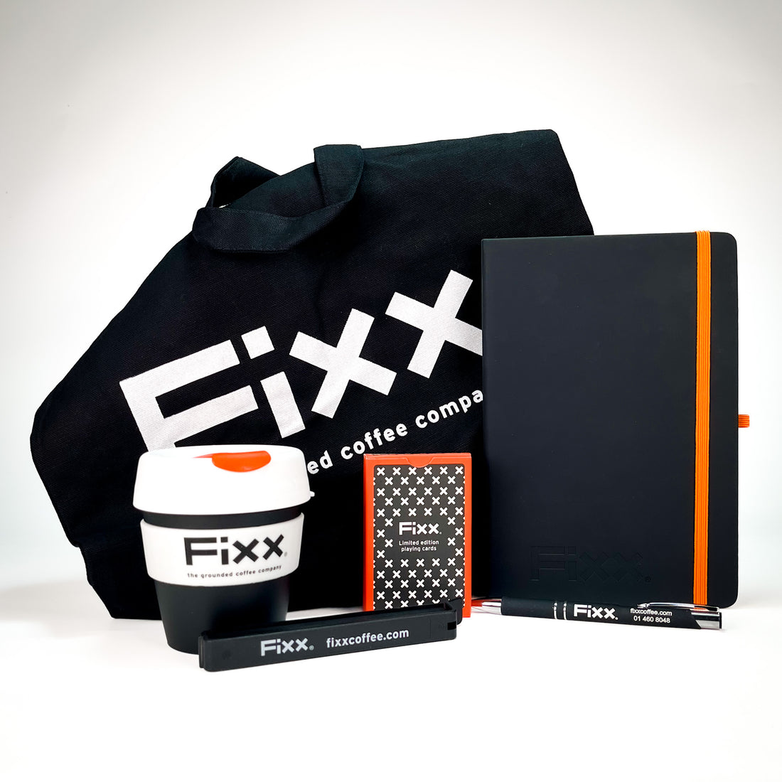 A branded coffee gift set on a white background, including a black tote bag, a black reusable coffee cup, a black notebook with an orange stripe, a small boxed item, and a black pen, all featuring the Fxx / fixcoffee branding.